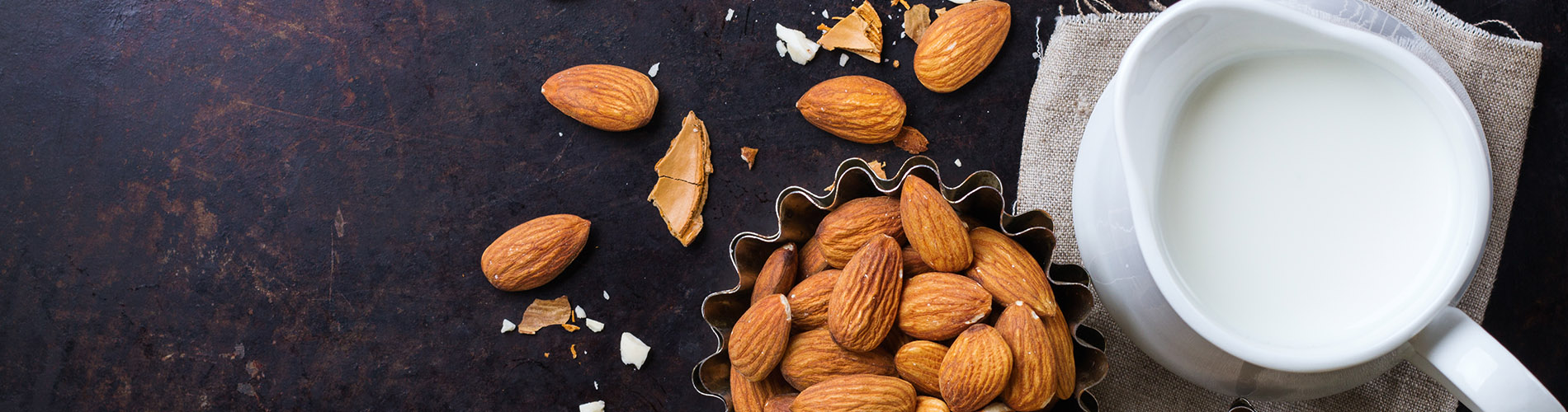 A bowl of almonds on a blue background with a pitcher of cream on the right.